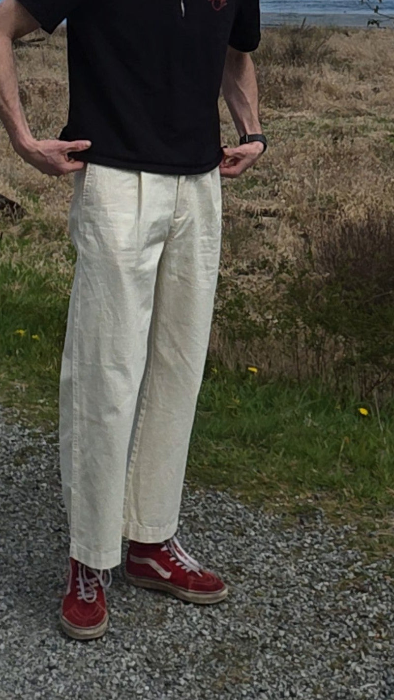 Person in white slacks standing on a gravel path with a scenic background of mountains and trees.
