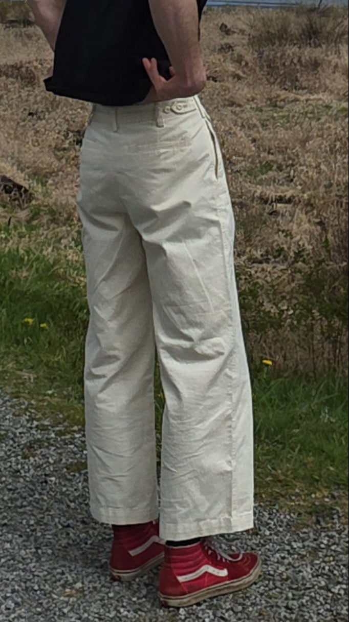 Person in white slacks standing on a gravel path with a scenic background of mountains and water.