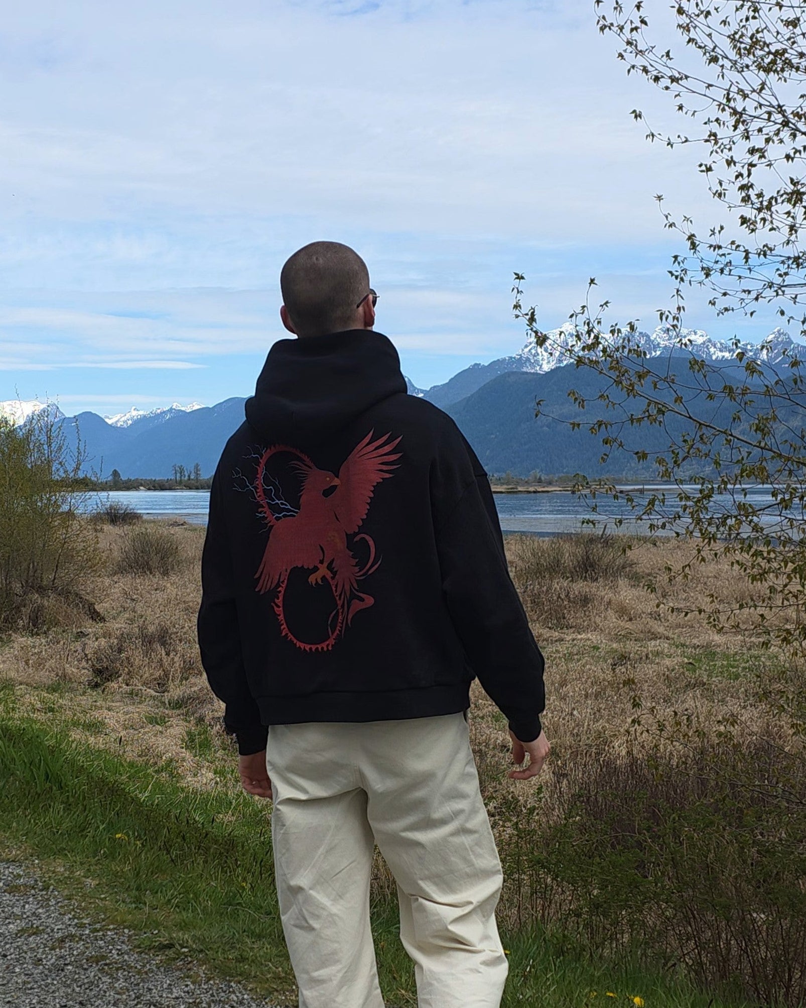 Person wearing the RISE Oversized Hoodie walking on a path with a scenic background of mountains and sky.