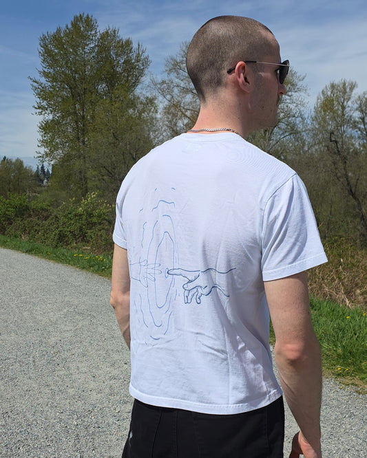 Man wearing a white ECHOES Basic Tee with a ripple design on the back, standing on a road with trees in the background.