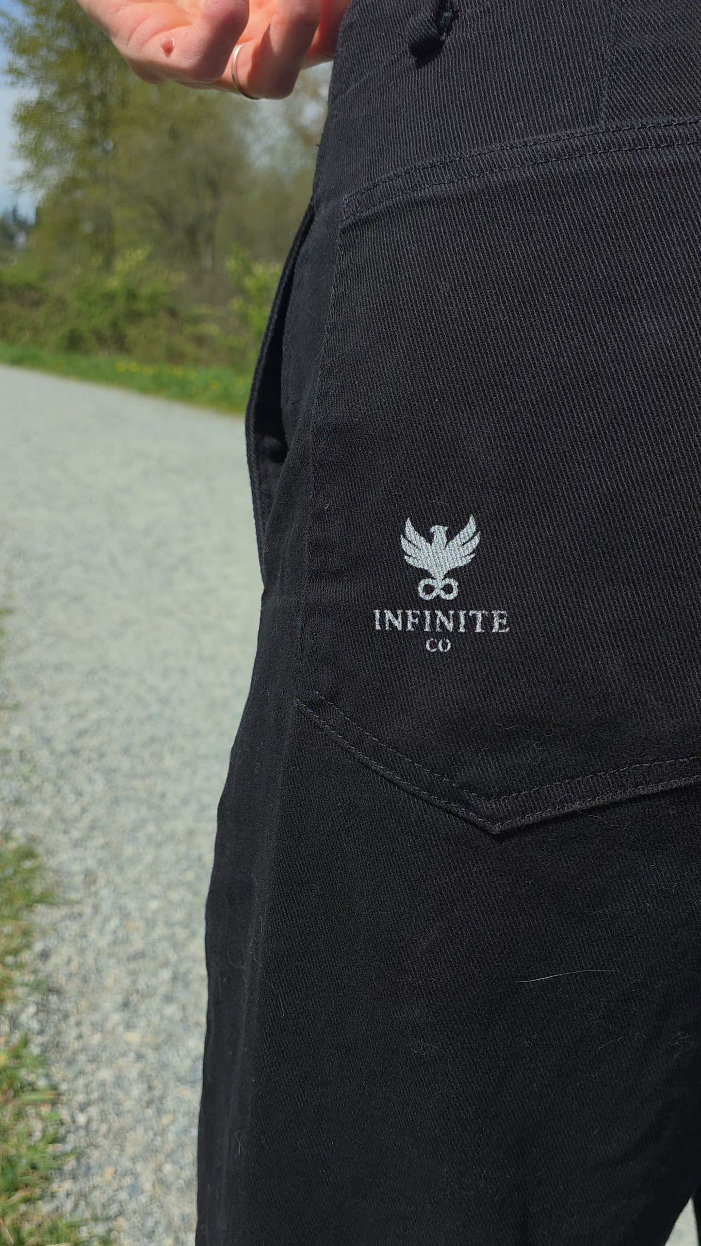 Black FUNDAMENTAL Barrel Leg Chinos with 'Infinite Co' logo on a blurred outdoor background