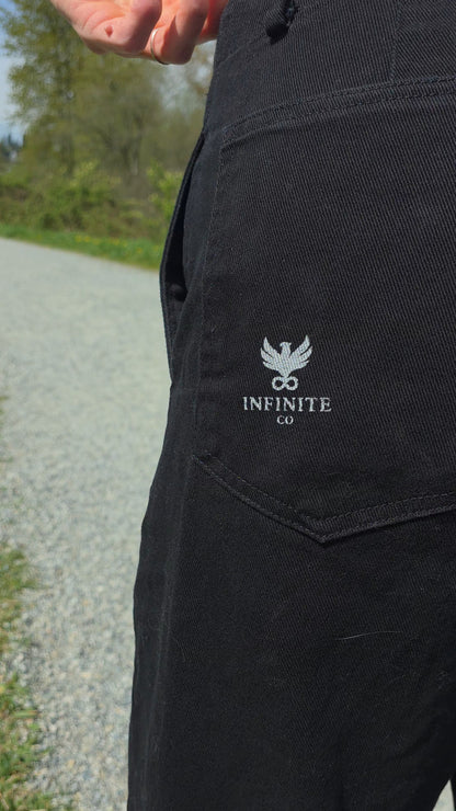 Black FUNDAMENTAL Barrel Leg Chinos with 'Infinite Co' logo on a blurred outdoor background