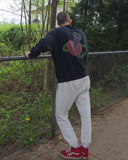 Person wearing a black sweatshirt with a colorful design, white ECHOES Cloud Comfort pants, and red shoes standing by a chain-link fence with trees in the background.