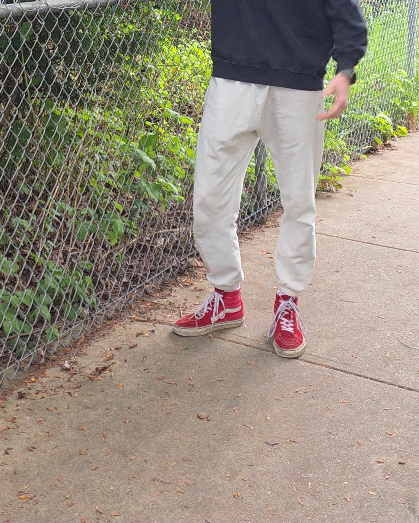 Man wearing ECHOES Cloud Comfort Pants standing by a chain-link fence with trees in the background