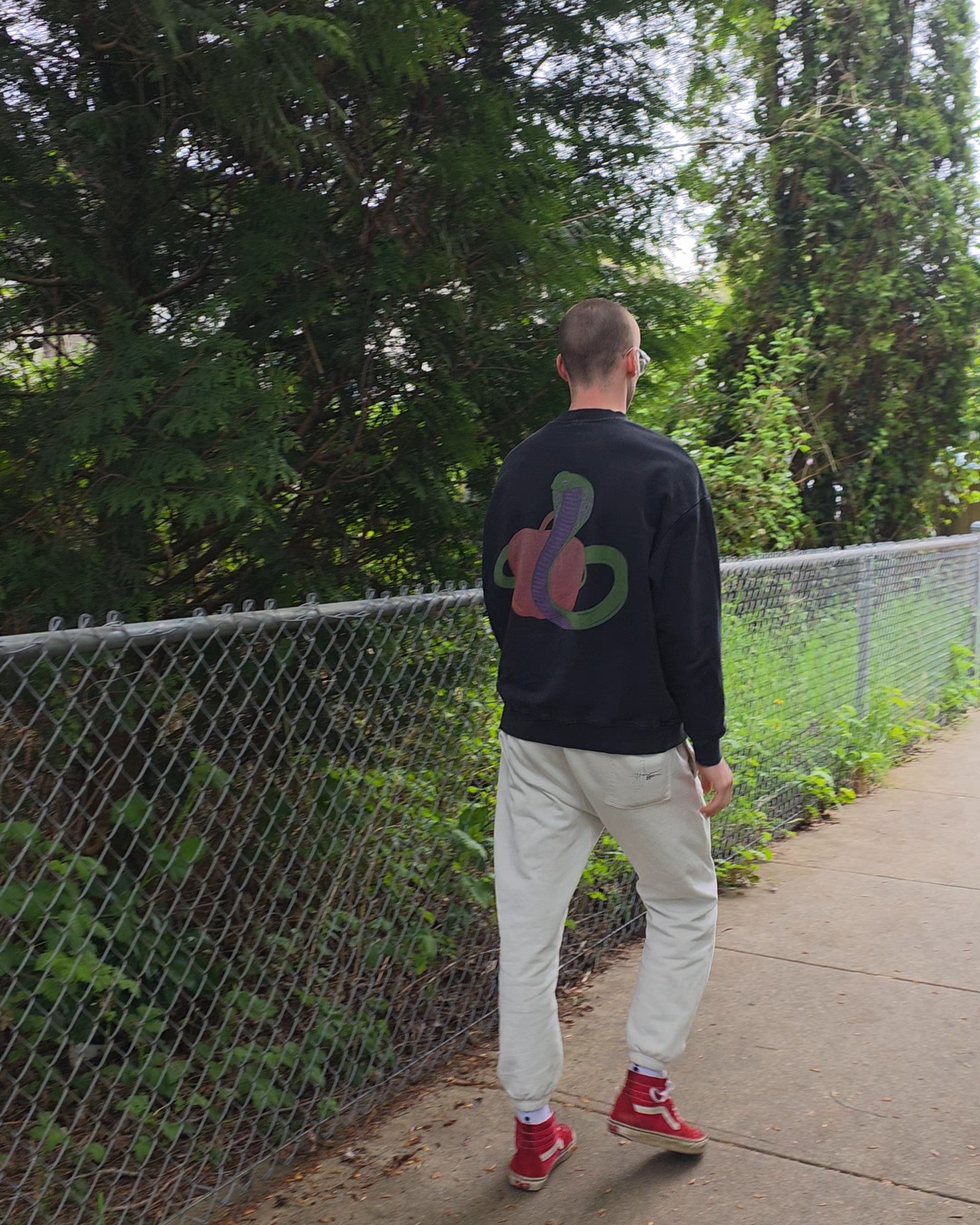 Person wearing EDEN Oversized Crewneck and ECHOES Cloud Comfort Pants walking on a path with trees and a fence in the background