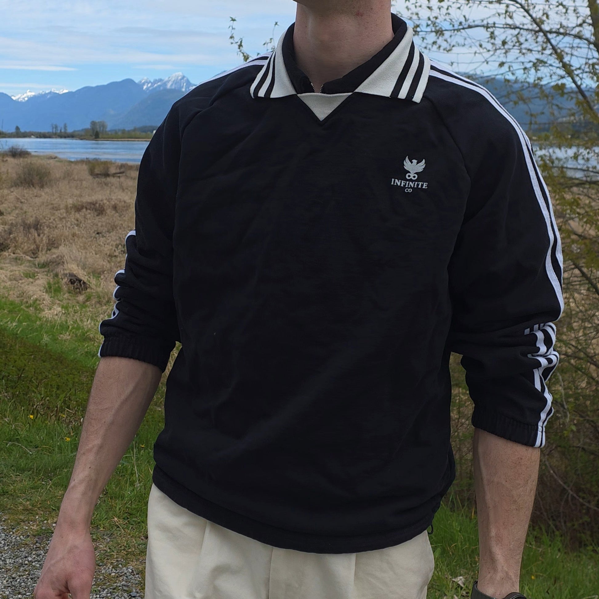 Man wearing a black sweater with a Infinite Co logo outdoors