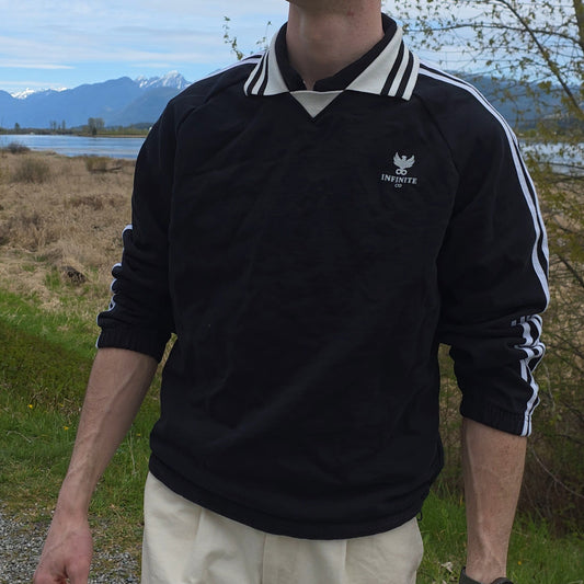 Man wearing a black sweater with a Infinite Co logo outdoors